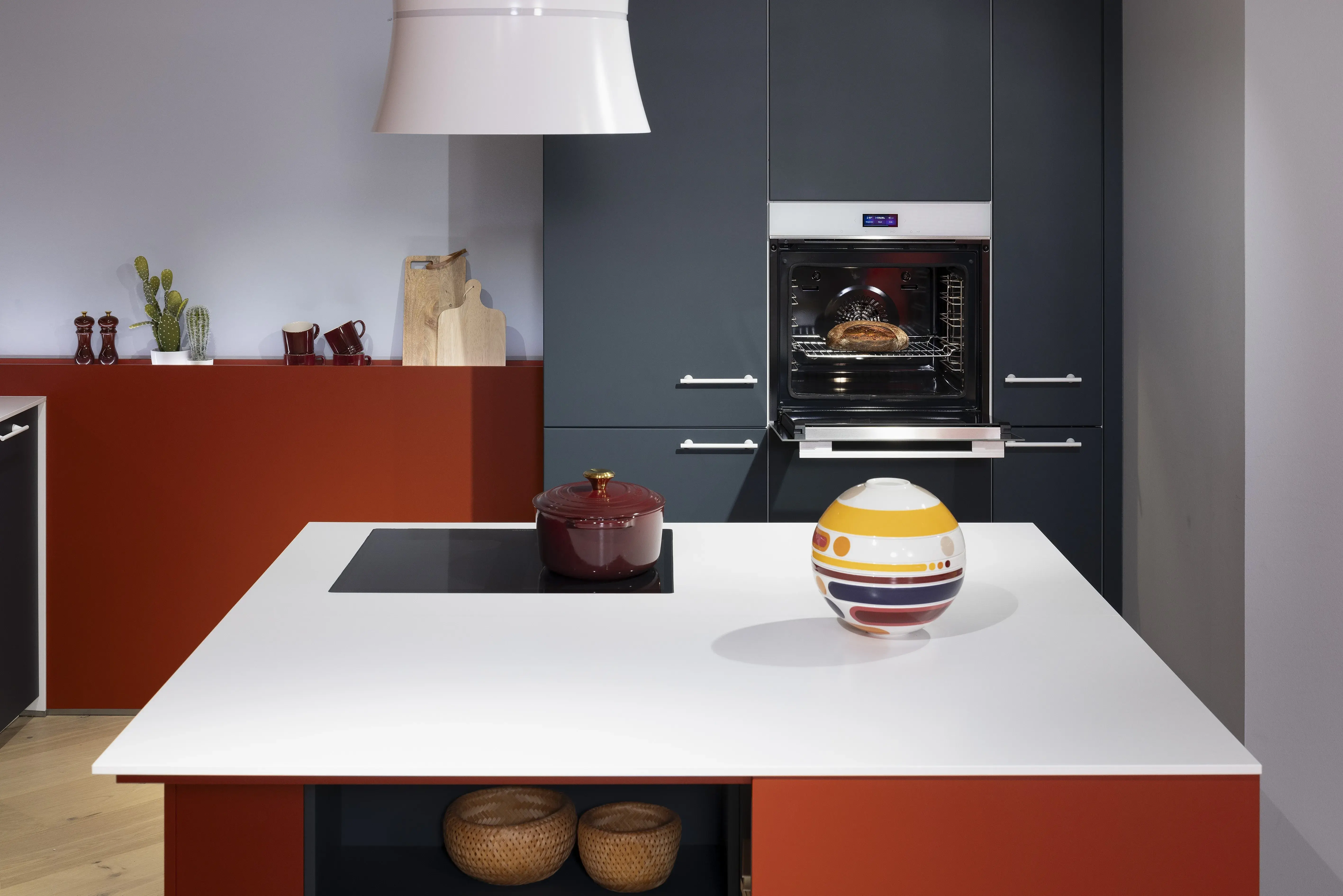 APL: Systeme Blanco Zeus matt Front: Herbstrot samtmatt AFP Front: Tiefblau samtmatt AFP Korpus: Kristallweiß/Naturweiß Griff: Metall Weiß lackiert Geräte: Siemens, Abzugshaube Airforce Armatur: Franke Spüle: Franke   Features: Farbe in der Küche, quadratische Kücheninsel mit Kochfeld und Dunstabzug, Kontrastelemente in Weiß (Griffe, APL, Spüle, Wasserhahn und Backofen), weißer BACKOFEN, kleine Designküche, junge Küche, Nischenrückwand als Motivfliese (Schüller), Arbeitsplatz, „versteckte“ Kaffeeküche 