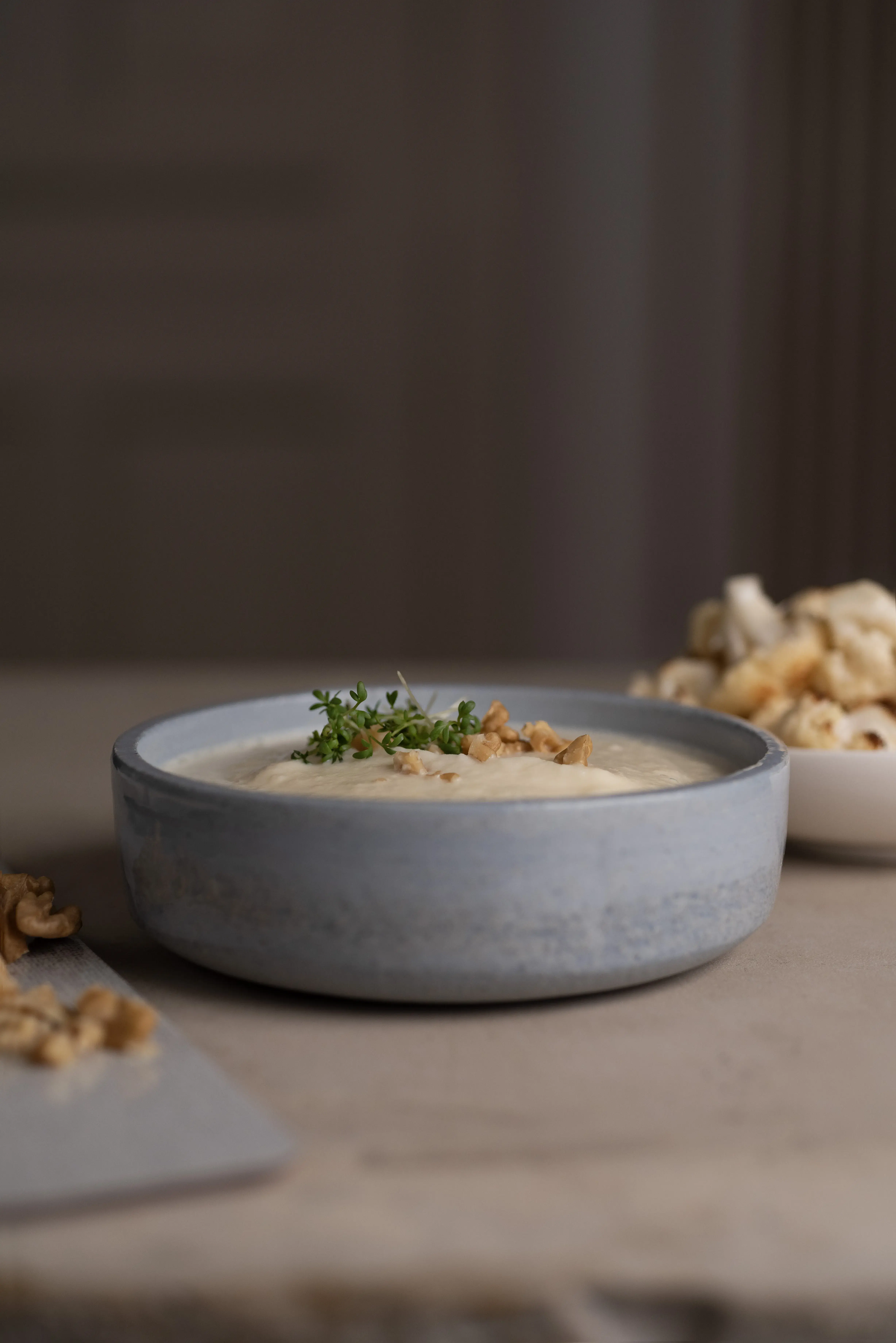 Cremige Suppe in grauer Schale, garniert mit Kräutern und Walnüssen.